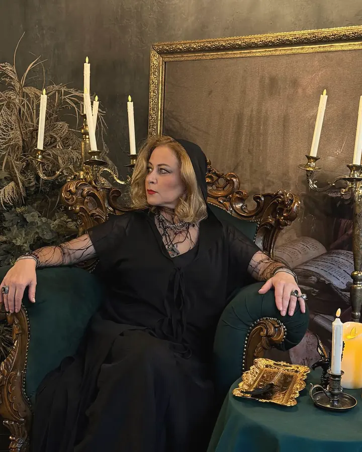 Alice in a carved green armchair among candles, looking away